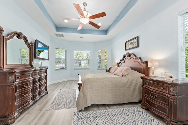 bedroom featuring ceiling fan, light hardwood / wood-style flooring, and a tray ceiling