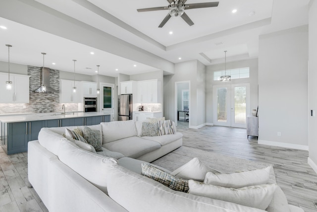 living room with a raised ceiling, light hardwood / wood-style flooring, sink, ceiling fan, and french doors