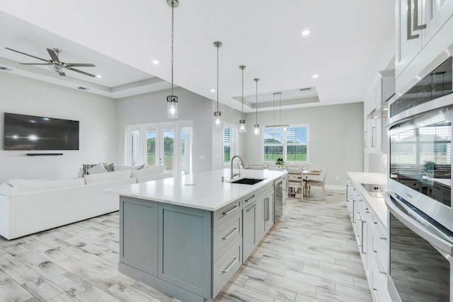 kitchen featuring a tray ceiling, sink, a center island with sink, and ceiling fan