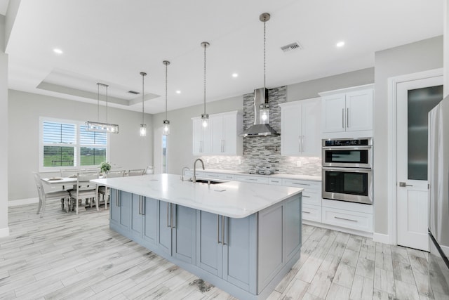 kitchen featuring a kitchen island with sink, a raised ceiling, white cabinetry, and decorative light fixtures