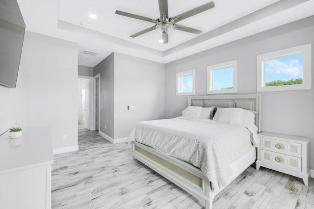 bedroom with a raised ceiling, ceiling fan, ensuite bath, and light hardwood / wood-style floors