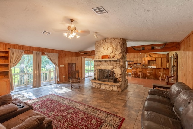 living room with a textured ceiling, wood walls, a fireplace, lofted ceiling, and ceiling fan