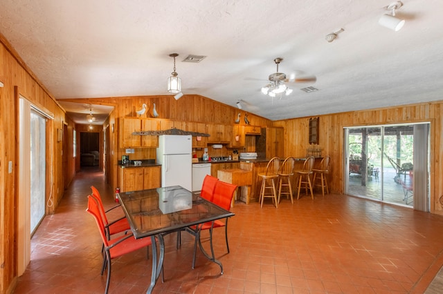 tiled dining space with vaulted ceiling, wooden walls, and ceiling fan