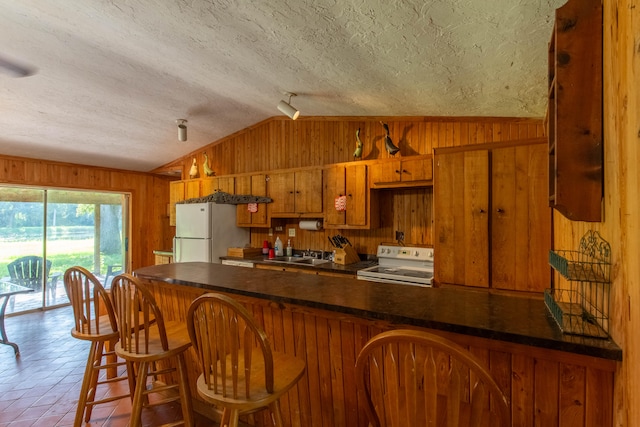 kitchen featuring a textured ceiling, kitchen peninsula, wood walls, and white appliances