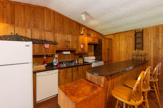 kitchen featuring white appliances, lofted ceiling, wood walls, a breakfast bar area, and a textured ceiling