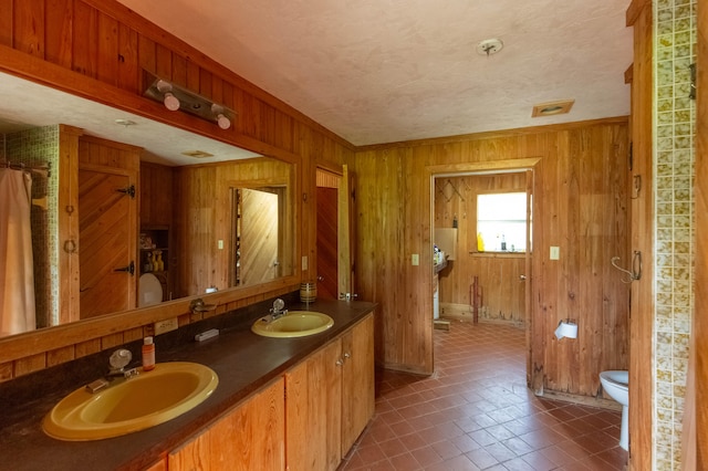 bathroom featuring toilet, vanity, a textured ceiling, wood walls, and a shower with curtain