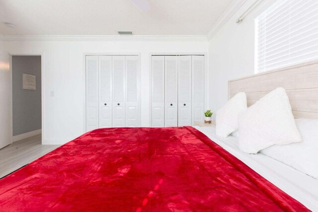 bedroom with ornamental molding, hardwood / wood-style floors, and two closets