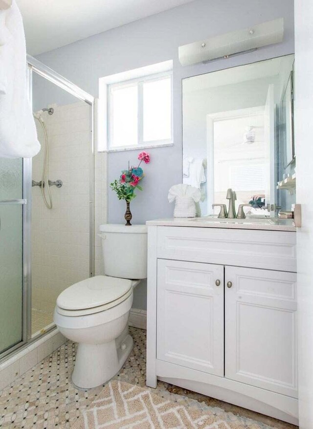 bathroom featuring a shower with door, vanity, and toilet