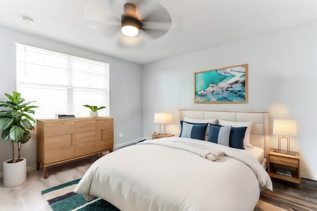 bedroom with ceiling fan, light hardwood / wood-style floors, and a baseboard heating unit