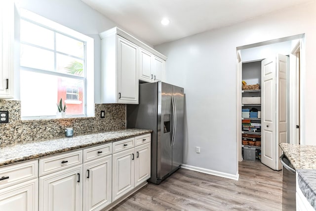 kitchen with stainless steel fridge with ice dispenser, white cabinetry, light stone counters, and light wood-type flooring