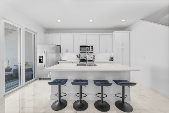 kitchen with appliances with stainless steel finishes, light tile patterned floors, a center island with sink, and white cabinetry