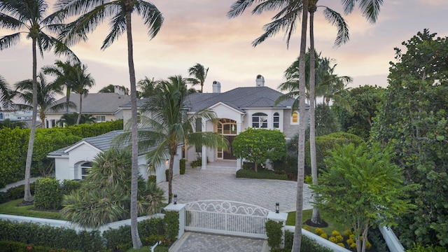 view of front facade with a fenced front yard, a tile roof, a chimney, stucco siding, and a gate