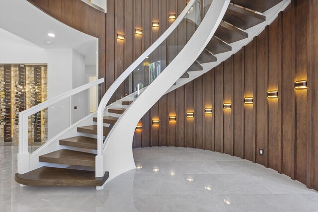 staircase featuring a towering ceiling, wooden walls, and tile patterned floors