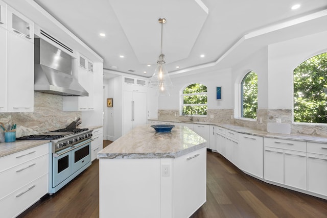 kitchen featuring a center island, white cabinets, double oven range, and wall chimney range hood