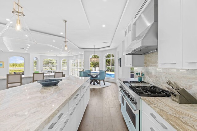 kitchen featuring wall chimney exhaust hood, stainless steel stove, tasteful backsplash, white cabinetry, and hardwood / wood-style flooring