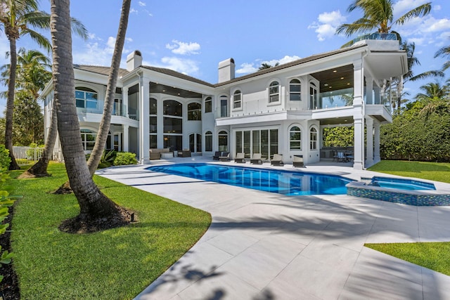 back of property with a balcony, a pool with connected hot tub, stucco siding, a chimney, and a patio area