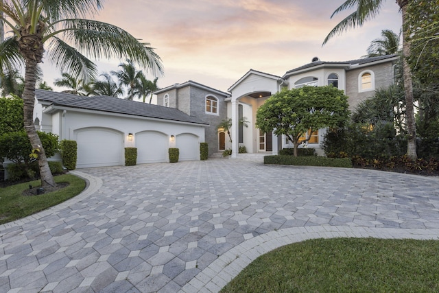 view of front of house featuring decorative driveway, an attached garage, a tile roof, and stucco siding