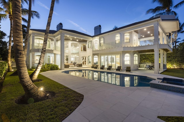 back of house with a balcony, a pool with connected hot tub, stucco siding, a chimney, and a patio area