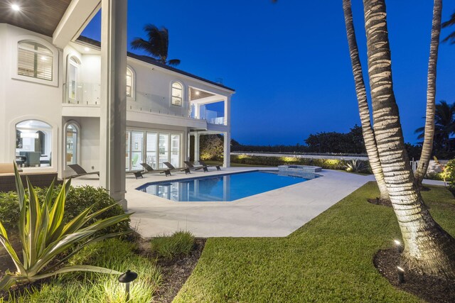 pool at night featuring a lawn and a patio area