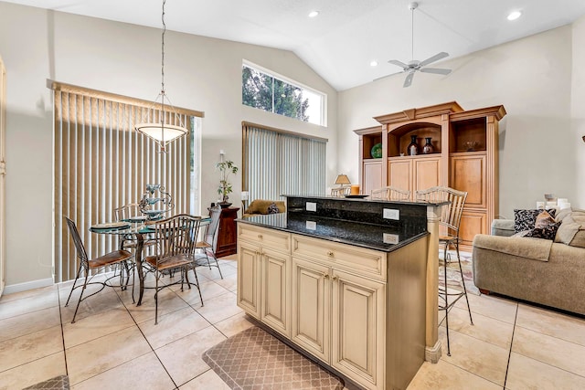 kitchen featuring dark stone countertops, light tile patterned floors, a center island, a kitchen breakfast bar, and ceiling fan