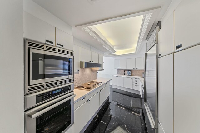 kitchen with appliances with stainless steel finishes, sink, white cabinets, backsplash, and a raised ceiling