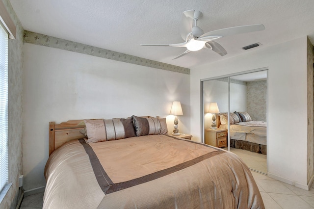 bedroom with light tile patterned floors, a textured ceiling, a closet, and ceiling fan