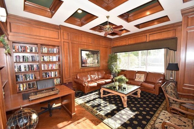 living area featuring beam ceiling, wooden walls, coffered ceiling, and ceiling fan