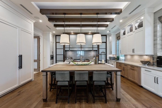 kitchen with dark wood-type flooring, beamed ceiling, an island with sink, and white cabinets