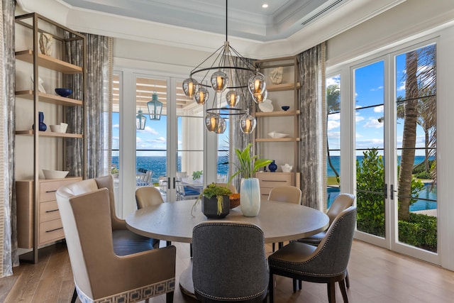 dining space with a notable chandelier, french doors, crown molding, light wood-type flooring, and a water view