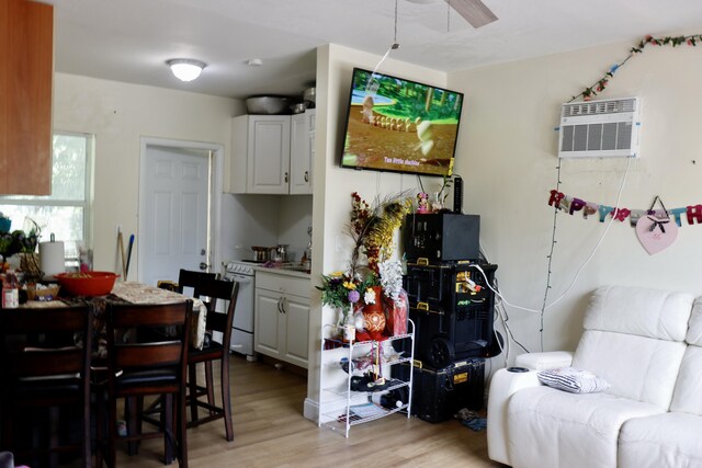 kitchen featuring an AC wall unit, light wood-style flooring, white range with electric stovetop, white cabinets, and ceiling fan