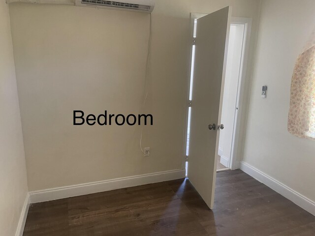 empty room with a wall mounted air conditioner, baseboards, and dark wood-style flooring