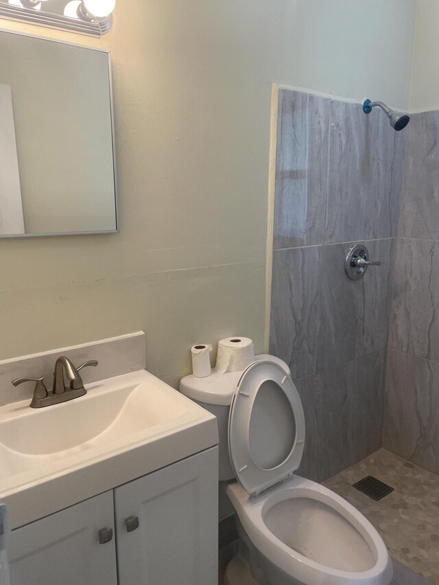 bathroom featuring toilet, tiled shower, and vanity