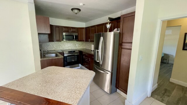 kitchen featuring tasteful backsplash, light countertops, light tile patterned floors, stainless steel appliances, and a sink