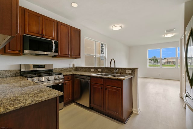 kitchen with stainless steel appliances, sink, light wood-type flooring, and dark stone counters