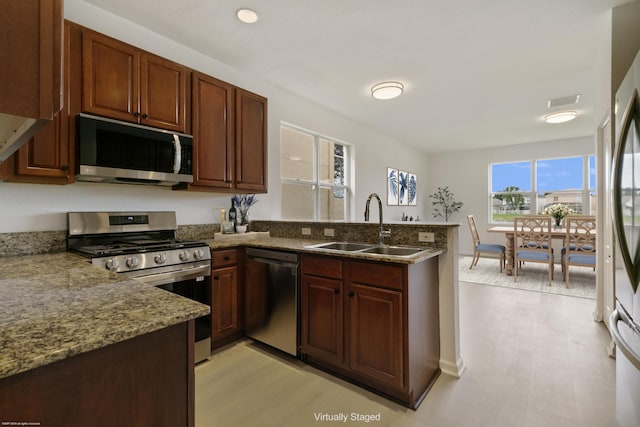 kitchen with dark stone countertops, light wood-type flooring, appliances with stainless steel finishes, sink, and kitchen peninsula