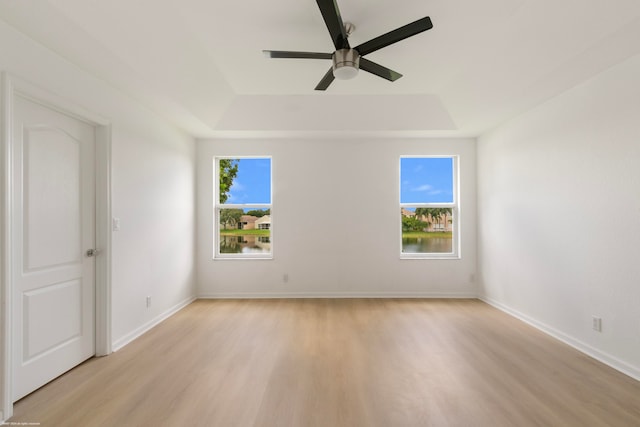 empty room featuring a wealth of natural light, a raised ceiling, ceiling fan, and light wood-type flooring