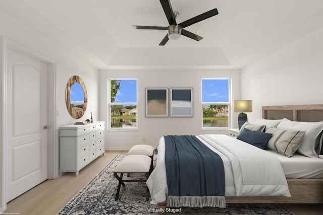 bedroom with a tray ceiling, ceiling fan, multiple windows, and light hardwood / wood-style floors