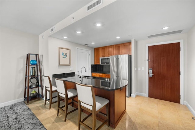 kitchen featuring decorative backsplash, a kitchen bar, appliances with stainless steel finishes, sink, and kitchen peninsula