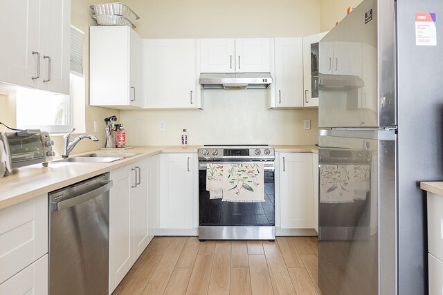 kitchen featuring appliances with stainless steel finishes, white cabinetry, sink, and light hardwood / wood-style flooring