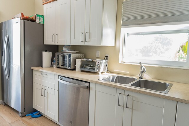 kitchen with sink, light hardwood / wood-style flooring, stainless steel appliances, and white cabinets