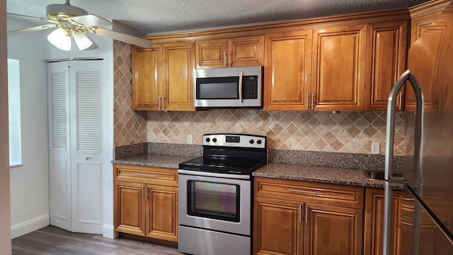 kitchen featuring dark hardwood / wood-style flooring, stainless steel appliances, ceiling fan, and dark stone countertops