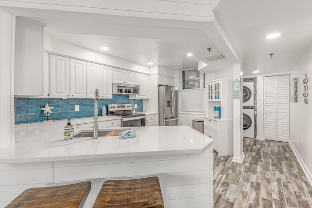 kitchen with backsplash, stacked washer / drying machine, appliances with stainless steel finishes, kitchen peninsula, and white cabinets