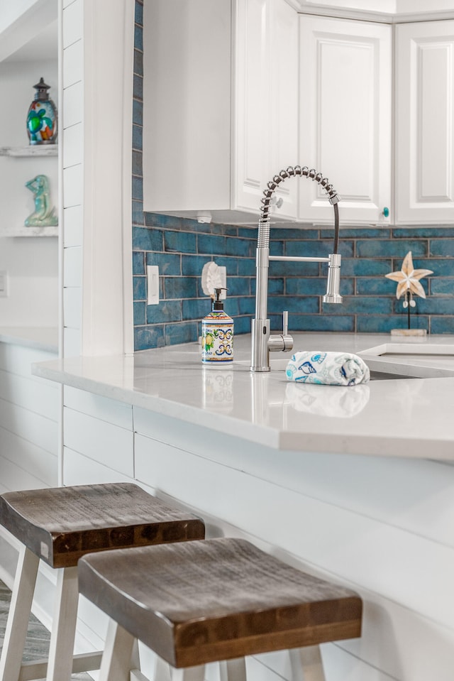 kitchen with a kitchen bar, decorative backsplash, and white cabinetry