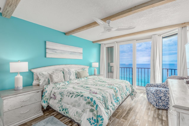 bedroom with a water view, wood-type flooring, ceiling fan, beam ceiling, and a textured ceiling