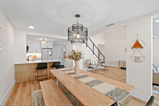 dining room with sink, a notable chandelier, and light hardwood / wood-style flooring