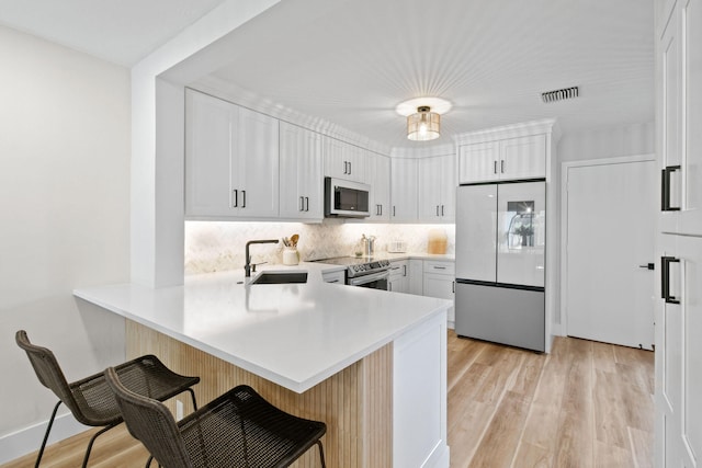 kitchen with light wood-type flooring, appliances with stainless steel finishes, sink, kitchen peninsula, and a kitchen breakfast bar