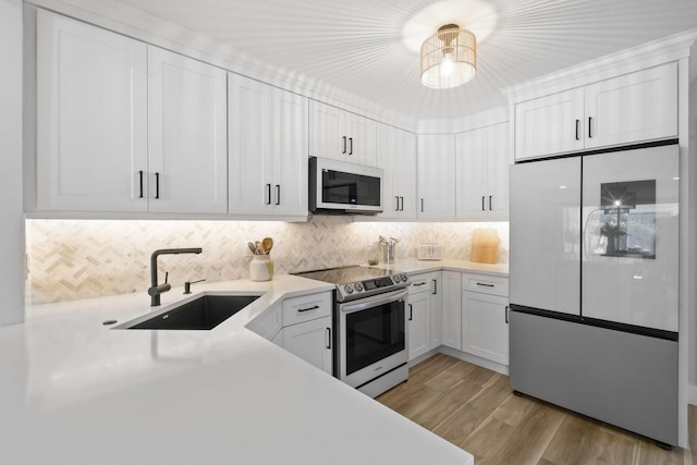 kitchen featuring white cabinets, appliances with stainless steel finishes, light hardwood / wood-style floors, sink, and decorative backsplash