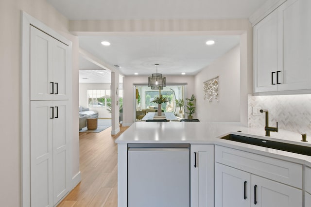 kitchen with white cabinetry, dishwasher, kitchen peninsula, sink, and light hardwood / wood-style floors