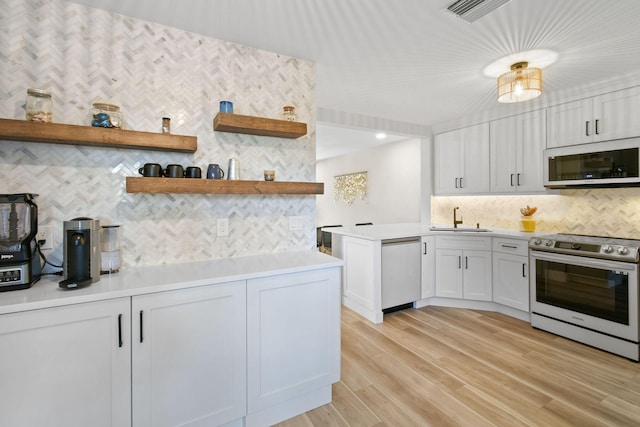 kitchen with appliances with stainless steel finishes, light hardwood / wood-style floors, white cabinetry, and sink