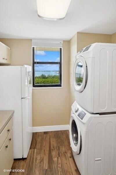 laundry room with dark wood-type flooring, stacked washer and clothes dryer, and cabinets